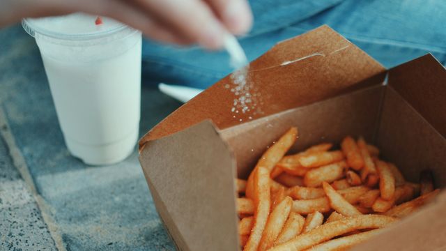 A person sprinkling salt onto a box of fries.