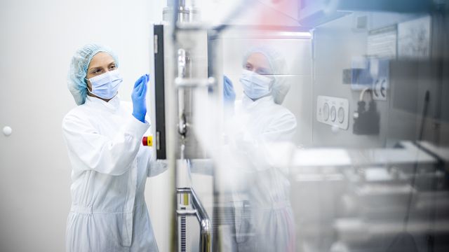 Scientist in protective clothing operating bioprocessing equipment in a sterile laboratory.