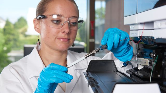 Scientist in lab coat and gloves performing maintenance on HPLC system in laboratory 