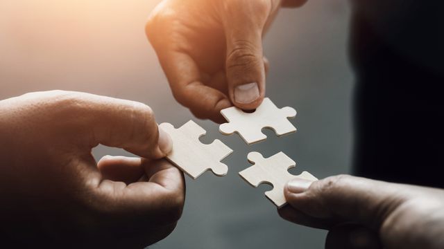 Three hands holding wooden jigsaw pieces together. 
