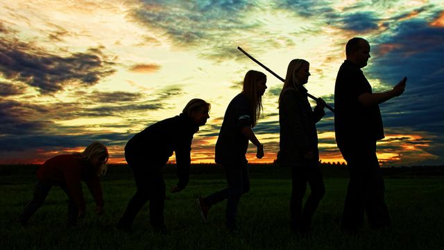 Silhouette sequence depicting human evolution from crouched posture to modern technology use against sunset.