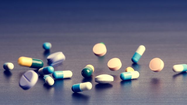 Various colorful pills and capsules scattered on a dark surface, including acetaminophen tablets.