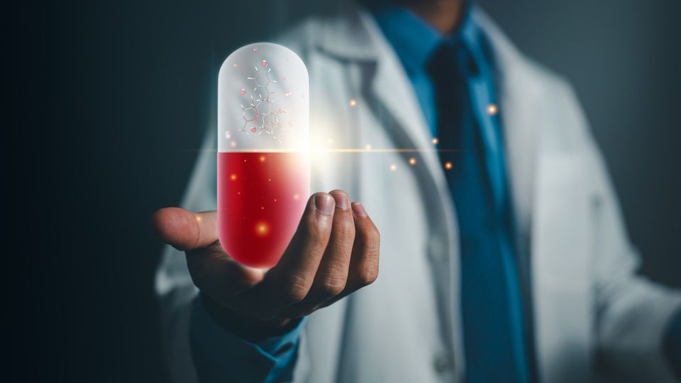 A person in a white lab coat "holding" an oversized red and white pill.