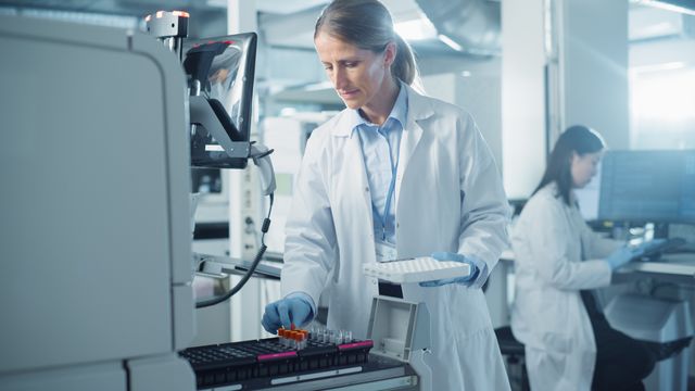Female scientist placing sample tubes into an automated lab analyzer in a modern laboratory. 