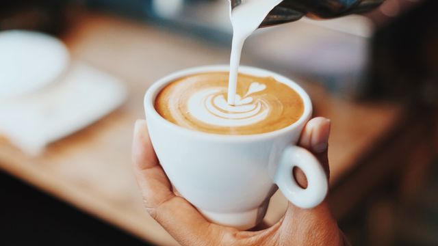 Barista pouring steamed milk into a cup of coffee, creating a heart-shaped latte art design.